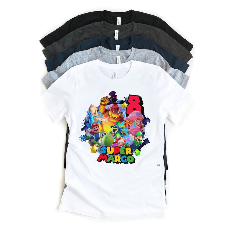 May include: A stack of t-shirts in various colors, including white, gray, navy, and black. The front white shirt features a colorful graphic of Super Mario characters with the text "Super Marco" and the number "8".