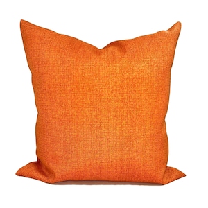 Puede incluir: Un cojín decorativo cuadrado de color naranja con una tela texturizada. El cojín tiene un color liso y un diseño sencillo, adecuado para la decoración del hogar. El cojín es de un tono naranja vibrante.