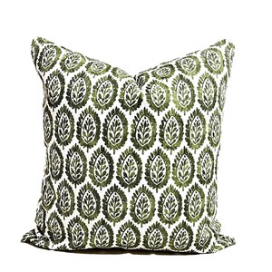 May include: Square decorative pillow with a white background and a repeating pattern of green leaf-shaped designs. The pillow has a soft, textured appearance, and the leaf pattern is detailed with varying shades of green.
