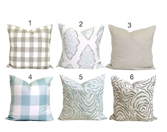 May include: Six decorative throw pillows with various patterns. The patterns include a gray and white plaid, a white and blue floral design, a solid beige, a blue and white plaid, a blue and white abstract design, and a gray and white zebra print.
