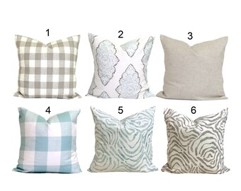 May include: Six decorative throw pillows with various patterns. The patterns include a gray and white buffalo check, a white damask with blue accents, a solid beige linen, a blue and white plaid, a blue and white watercolor zebra print, and a gray and white zebra print.