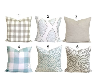 May include: Six decorative throw pillows with various patterns. The patterns include a gray and white buffalo check, a white damask with blue accents, a solid beige linen, a blue and white plaid, a blue and white watercolor zebra print, and a gray and white zebra print.