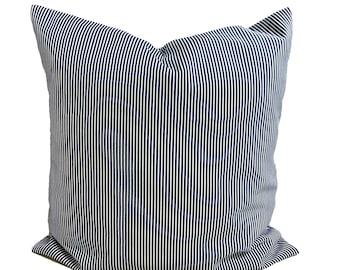 May include: A square pillow with a navy blue and white striped pattern. The pillow has a soft, plush appearance and is likely made of fabric. The stripes are vertical and evenly spaced, creating a classic, nautical aesthetic.