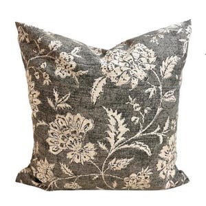 May include: A square cushion with a dark grey backdrop and a cream floral design. The cushion showcases a detailed botanical pattern with large flowers and leaves, ideal for home decoration.