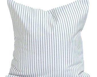May include: A square pillow with a white background and vertical gray stripes. The pillow is made of a soft fabric and is designed for decorative use on a bed or sofa. The pillow is a neutral color and can match any decor.