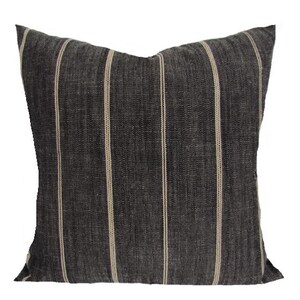 Puede incluir: Un cojín decorativo cuadrado con tela gris oscuro y rayas verticales color crema. El cojín tiene una apariencia texturizada y está diseñado para la decoración del hogar.