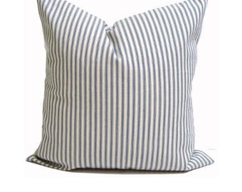May include: Square pillow with a white background and vertical blue stripes. The pillow has a soft, textured appearance and is likely made of fabric. The pillow is a decorative item for a bed or sofa.