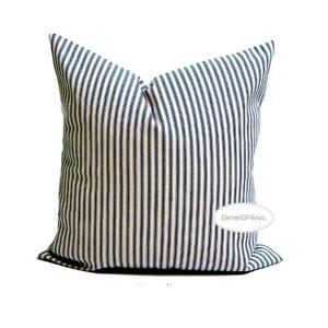 Puede incluir: Un cojín cuadrado con rayas verticales azul marino y blancas. El artículo es un elemento decorativo, probablemente para una cama o un sofá. La tela tiene un aspecto suave y texturizado.