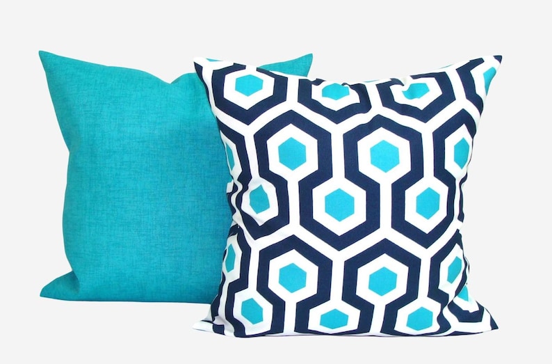 May include: Two decorative throw pillows. One is solid turquoise, the other features a geometric pattern of navy blue, white, and turquoise hexagons. The pillows are square and appear to be made of a textured fabric.