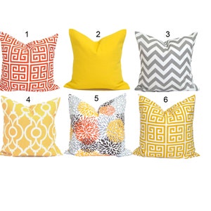 K&ouml;nnte beinhalten: Sechs dekorative Zierkissen in verschiedenen Farben und Mustern. Designs umfassen ein rot-wei&szlig;es geometrisches Muster, einfarbiges Gelb, graues Zickzack, gelbes und wei&szlig;es Gitter, Blumenmuster und ein goldfarbenes geometrisches Muster.