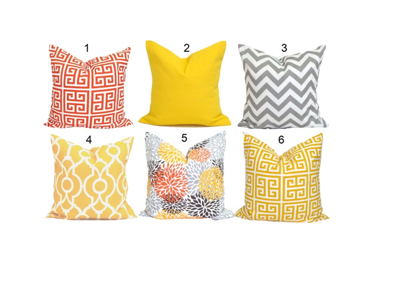 K&ouml;nnte beinhalten: Sechs dekorative Zierkissen in verschiedenen Farben und Mustern. Designs umfassen ein rot-wei&szlig;es geometrisches Muster, einfarbiges Gelb, graues Zickzack, gelbes und wei&szlig;es Gitter, Blumenmuster und ein goldfarbenes geometrisches Muster.