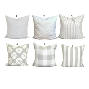 May include: Six decorative cushions in various patterns. Designs include a geometric weave, textured solid, vertical stripes, floral, buffalo check, and wide vertical stripes. The cushions are primarily in shades of grey and white.