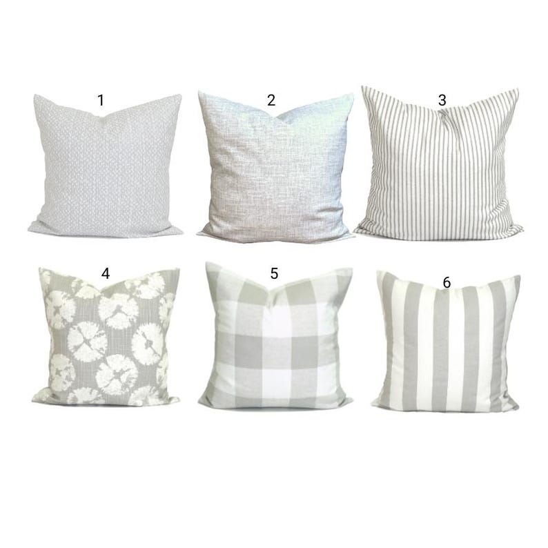 May include: Six decorative cushions in various patterns. Designs include a geometric weave, textured solid, vertical stripes, floral, buffalo check, and wide vertical stripes. The cushions are primarily in shades of grey and white.