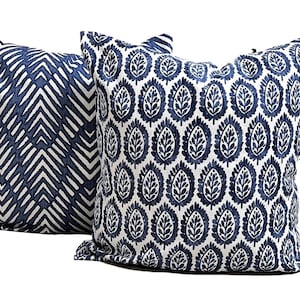 Pu&ograve; includere: Due cuscini decorativi quadrati. Uno presenta un motivo a chevron blu navy e bianco, l'altro un motivo a foglie blu navy ripetuto su sfondo bianco. I cuscini sono in tessuto e sono adatti per un divano o un letto.