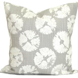 May include: A square cushion featuring a light grey backdrop with a repeating pattern of large, white, abstract floral shapes. The cushion has a soft, textured appearance, suitable for home decor.