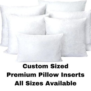 May include: Five white pillow inserts of various sizes, stacked on top of each other. The text "Custom Sized Premium Pillow Inserts All Sizes Available" is printed below the pillows.
