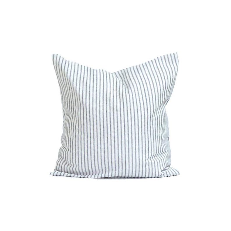 May include: A square pillow with a white background and vertical gray stripes. The pillow is made of fabric and has a soft, textured appearance. The pillow is a decorative item for a bed or sofa.