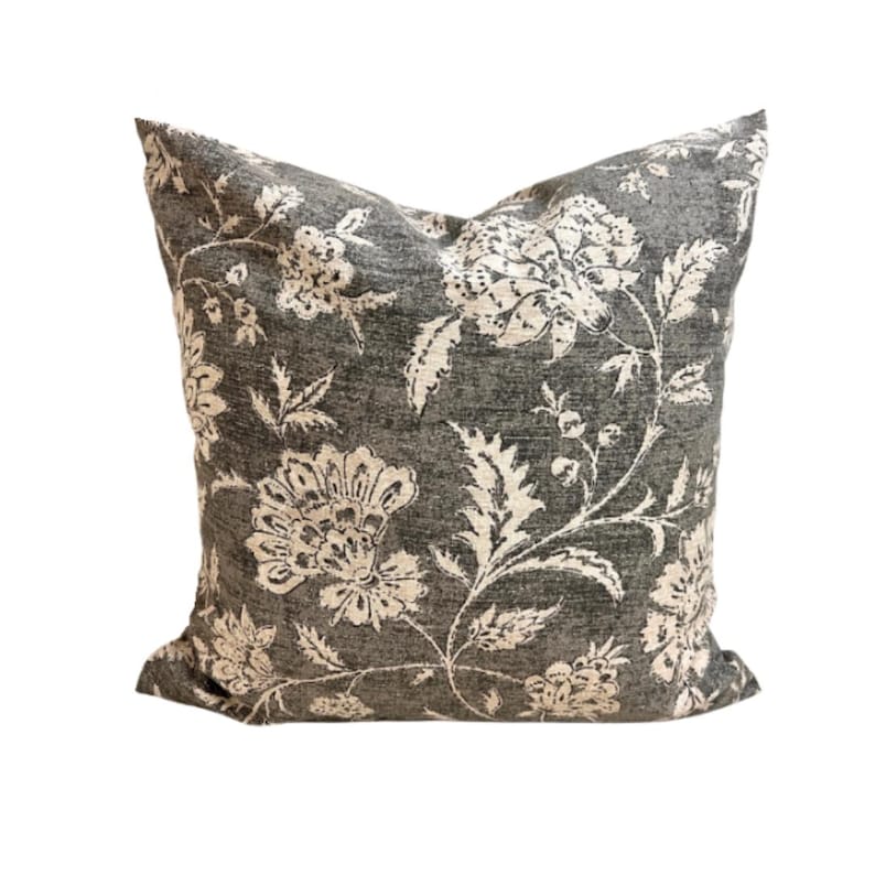 May include: A square throw pillow featuring a dark charcoal gray fabric base with a contrasting cream-colored floral pattern. The design displays large, intricate blossoms, leaves, and stems spread across the entire surface of the pillow cover.