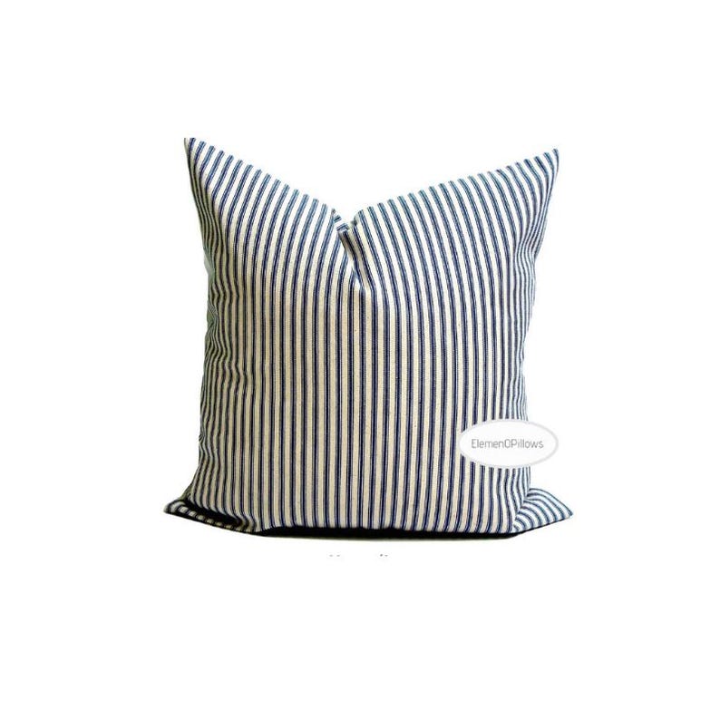 May include: A square pillow with a white background and a navy blue stripe pattern. The pillow is a decorative item, likely for a bed or sofa. The pillow has a soft, textured appearance.