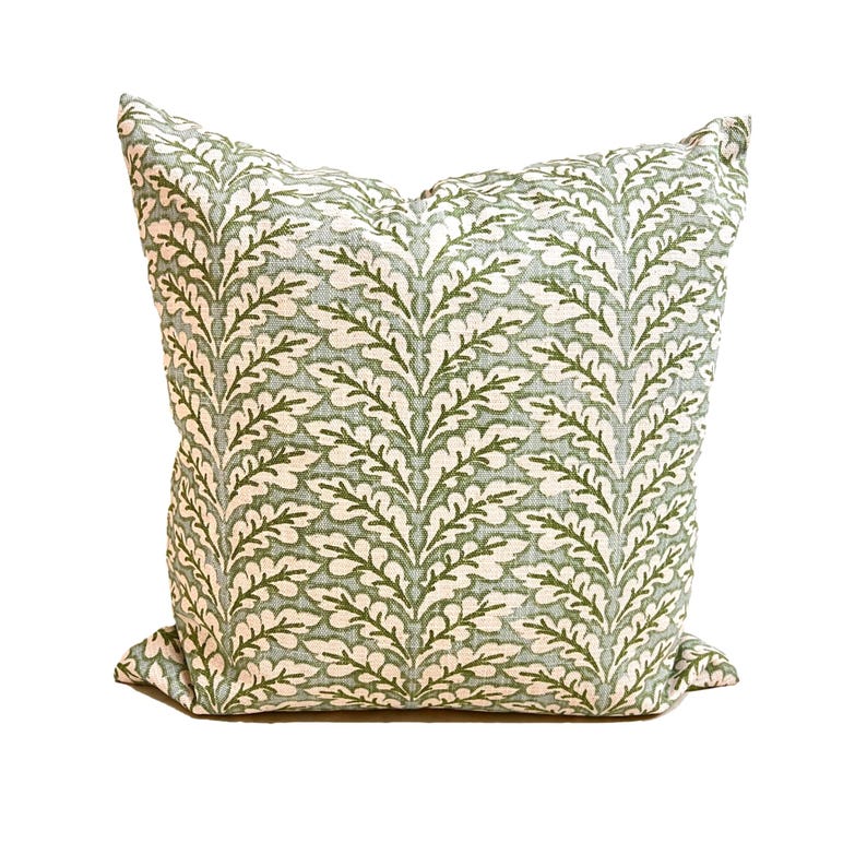 May include: A square throw pillow featuring a repeating vertical pattern of dark green oak leaves on a light sage green background. The fabric has a visible woven texture, and the pillow is filled to create a plump, soft, and structured shape.