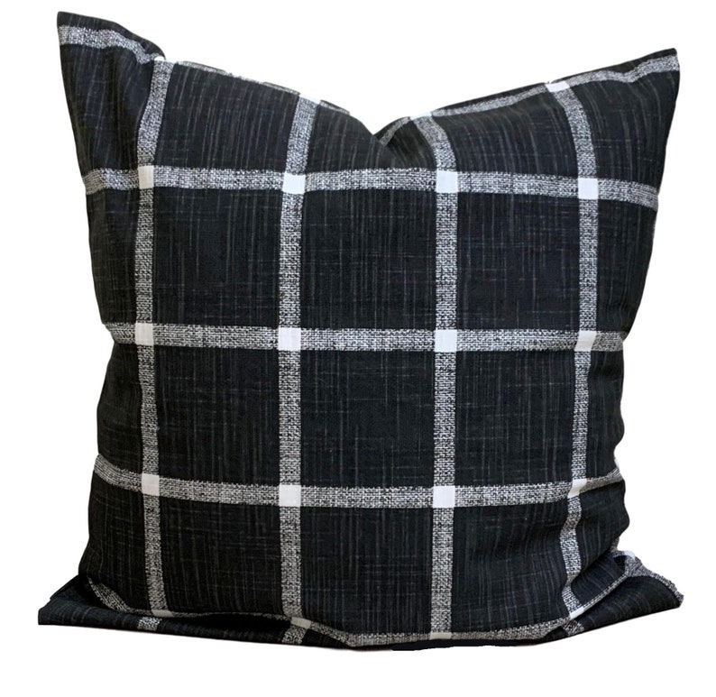 May include: Square cushion with a black and white check pattern. The cushion has a dark background with a grid of white lines and squares, creating a classic design. A soft, comfortable home decor item, suitable for a sofa or bed.