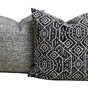 May include: Two square throw cushions. One is grey with a textured weave, the other has a black and white geometric design. The cushions are made of a soft fabric, suitable for a sofa or bed.
