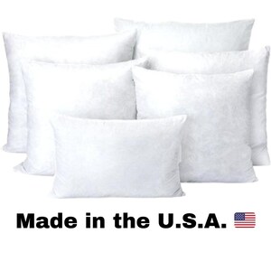 May include: A collection of white, fluffy pillows of various sizes. The pillows are arranged in a group, with some overlapping. The text "Made in the U.S.A." is displayed below the pillows, accompanied by a small American flag.