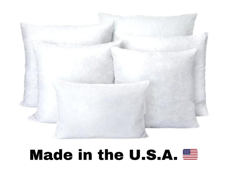 May include: A collection of white, fluffy pillows of various sizes. The pillows are arranged in a group, with some overlapping. The text "Made in the U.S.A." is displayed below the pillows, accompanied by a small American flag.