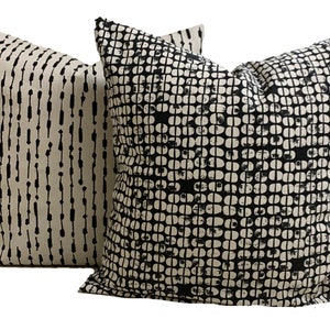 May include: Two decorative throw pillows with abstract patterns. One pillow features vertical black lines on a beige background. The other pillow has a black and white geometric pattern, resembling a series of connected circles.