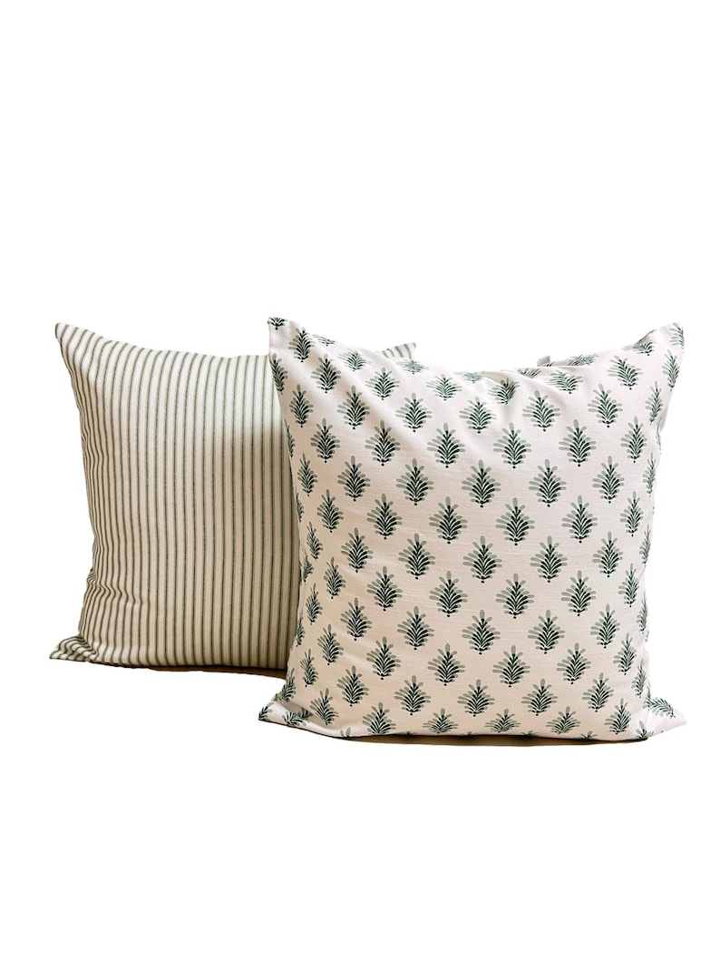 May include: Two square throw pillows. The front pillow features a white background with a repeating dark green botanical leaf pattern. The back pillow features a white background with thin, vertical dark green stripes across the entire surface.
