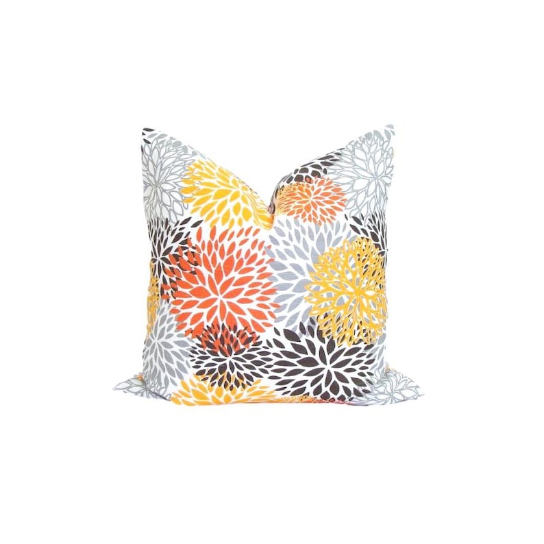 Puede incluir: Un coj&iacute;n decorativo cuadrado con un estampado floral repetido en amarillo, naranja, gris y negro sobre un fondo blanco. Este coj&iacute;n decorativo es un art&iacute;culo de decoraci&oacute;n del hogar.