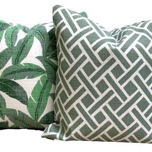 May include: Two decorative throw pillows. One features a tropical leaf pattern in shades of green on a white background. The other has a geometric trellis design in green and white. These pillows add a touch of nature and style to any room.