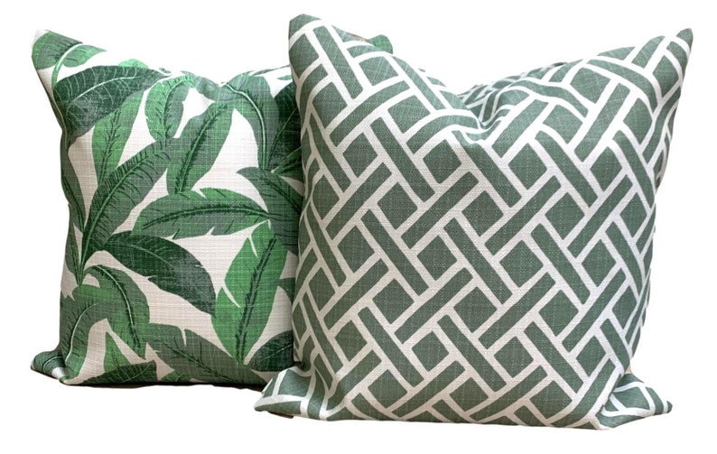 May include: Two decorative throw pillows. One features a tropical leaf pattern in shades of green on a white background. The other has a geometric trellis design in green and white. These pillows add a touch of nature and style to any room.