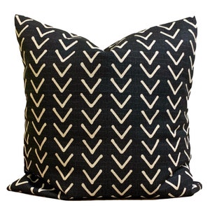 May include: Square cushion featuring a black fabric with a repeating pattern of off-white chevrons. The cushion has a textured appearance. The design is modern and suitable for home decor. The cushion is likely made of fabric.