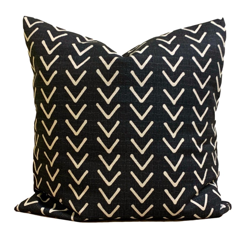 May include: Square cushion featuring a black fabric with a repeating pattern of off-white chevrons. The cushion has a textured appearance. The design is modern and suitable for home decor. The cushion is likely made of fabric.