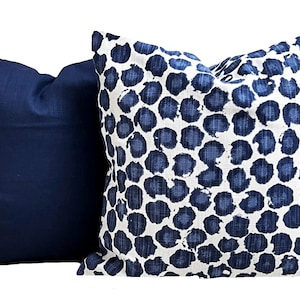 Pu&ograve; includere: Due cuscini decorativi quadrati. Uno &egrave; blu navy tinta unita, l'altro presenta uno sfondo bianco con un motivo a pois blu navy. I cuscini sono in tessuto e sono destinati all'arredamento.