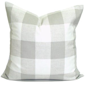 May include: A square cushion featuring a large buffalo check pattern in white and light grey. The cushion has a soft, textured appearance and is designed for home decor.