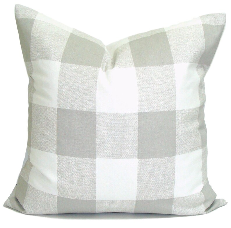 May include: A square cushion featuring a large buffalo check pattern in white and light grey. The cushion has a soft, textured appearance and is designed for home decor.