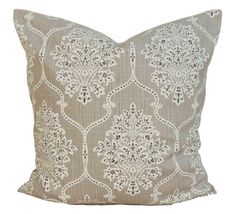 May include: A square cushion featuring a beige backdrop and a repeating white and dark brown floral design. The cushion has a textured look and a classic pattern, suitable for home decor.