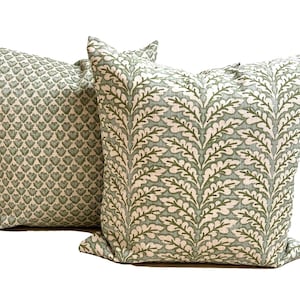 May include: Two square throw pillows featuring a light green and cream color palette. The front pillow displays a vertical repeating leaf pattern, while the back pillow features a dense, small-scale heart-shaped motif in the same color scheme.