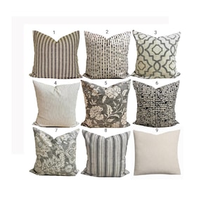 May include: A collection of nine square throw pillows arranged in a grid, featuring various patterns including vertical stripes, geometric lattice, floral motifs, and a solid beige option, all in neutral shades of black, white, grey, and cream.