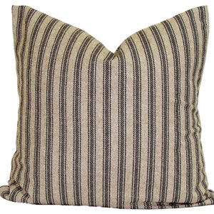 May include: A square decorative pillow with a beige background and vertical black stripes. The pillow has a soft, textured appearance and is likely made of fabric. The pillow is designed for home decor.