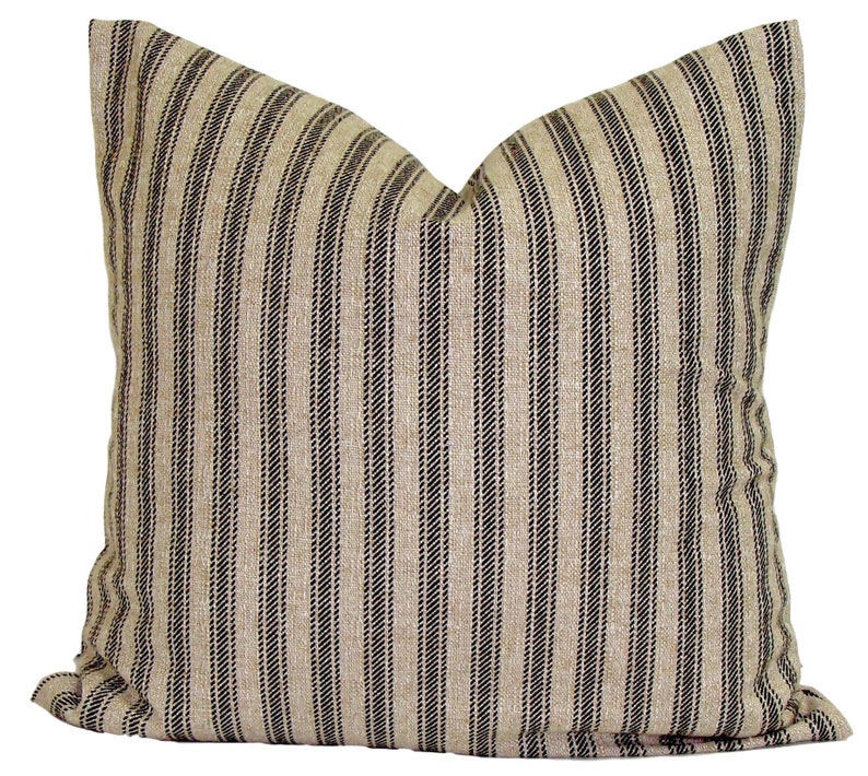 May include: A square decorative pillow with a beige background and vertical black stripes. The pillow has a soft, textured appearance and is likely made of fabric. The pillow is designed for home decor.
