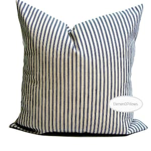 May include: A square throw pillow featuring a vertical striped pattern in dark navy blue and off-white. The fabric has a visible woven texture. A white oval label with the text ElemenOPillows is positioned on the lower right side of the pillow.