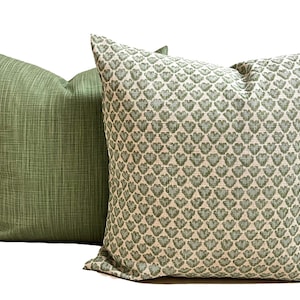 May include: Two square throw pillows. The pillow on the left is a solid sage green with a subtle cross-hatch texture. The pillow on the right features a repeating pattern of small, sage green heart-shaped motifs on a light cream-colored background.