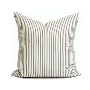 May include: A square throw pillow featuring a classic ticking stripe pattern with thin, dark charcoal-colored vertical lines set against a crisp, off-white fabric background. The pillow has a structured, plump appearance with clean, finished edges.