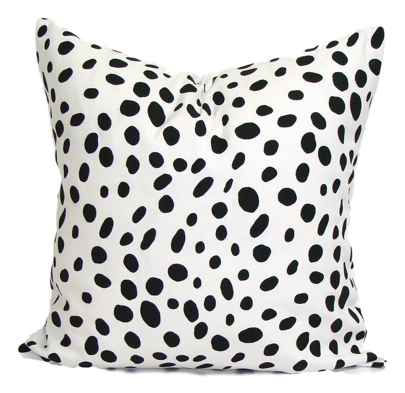 May include: Square decorative pillow with a white background and a pattern of black, irregular spots. The pillow is a solid color on the back. The pillow is a square shape.