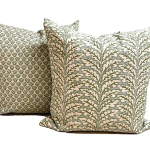 May include: Two square throw pillows featuring a textured fabric with a light green and white color scheme. One pillow displays a dense pattern of small heart-shaped motifs, while the other showcases a repeating vertical fern leaf design.