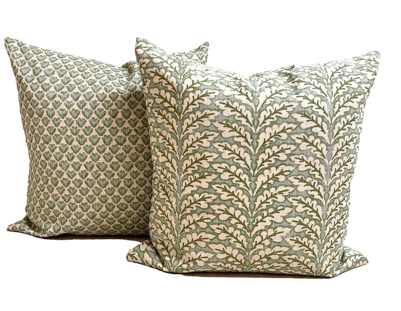 May include: Two square throw pillows featuring a textured fabric with a light green and white color scheme. One pillow displays a dense pattern of small heart-shaped motifs, while the other showcases a repeating vertical fern leaf design.