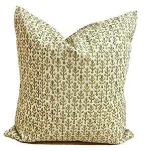 May include: A square throw pillow featuring a repeating pattern of small, stylized green leaf motifs printed on a textured, off-white fabric base. The pillow has a plump, filled appearance with visible seams along the edges and a woven textile finish.